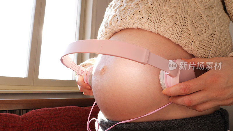 在家的孕妇把耳机戴在肚子上，让宝宝听她肚子里的音乐，孕期的娱乐活动