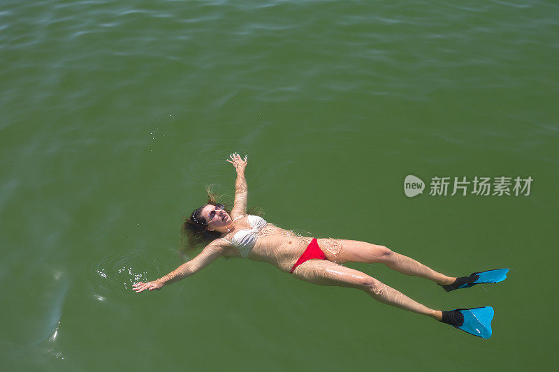 年轻女子仰面在海里游泳。
