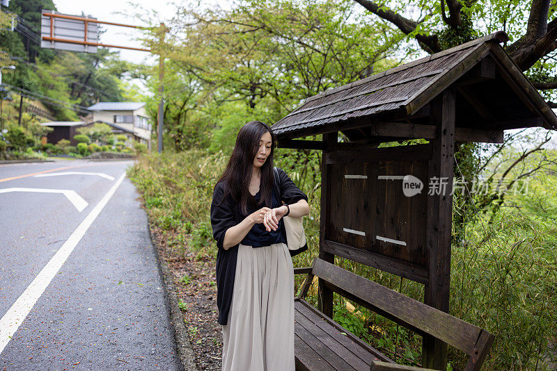 一名日本妇女在旅游地点等车，用手表看时间