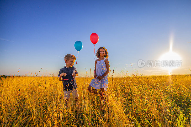 微笑的兄弟姐妹拿着气球，在草地上对着天空玩耍