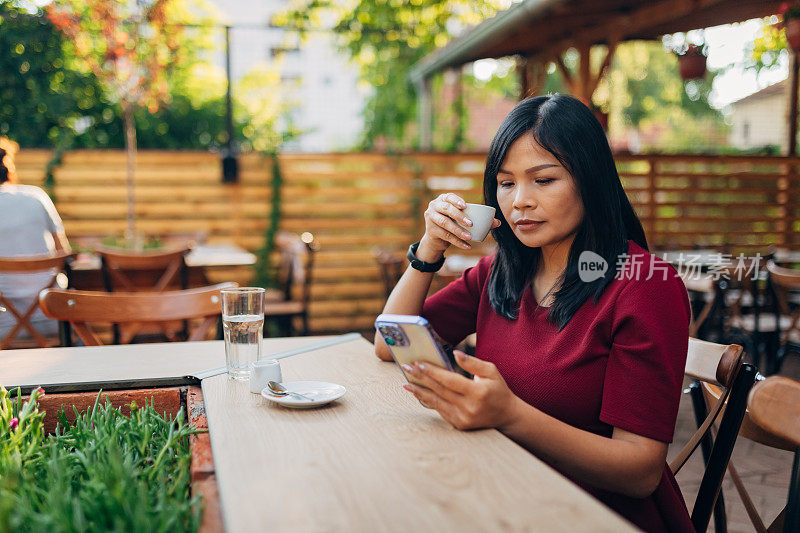 一位女交易员正在咖啡店里喝着咖啡，用着手机休息