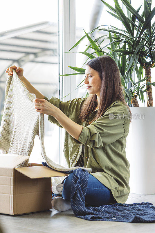 垂直照片，一名女子正在查看她在网上买的衣服，把它们从盒子里拿出来
