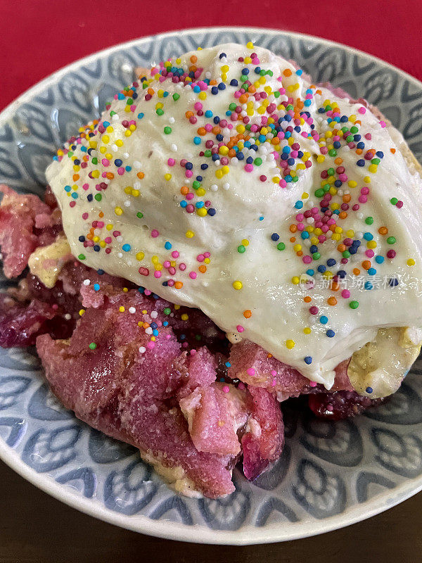 蓝色盘子的特写图片，上面点缀着鲜奶油和彩虹多色糖屑，多层海绵蛋糕，蛋奶和草莓果冻，粉红色背景，高视图