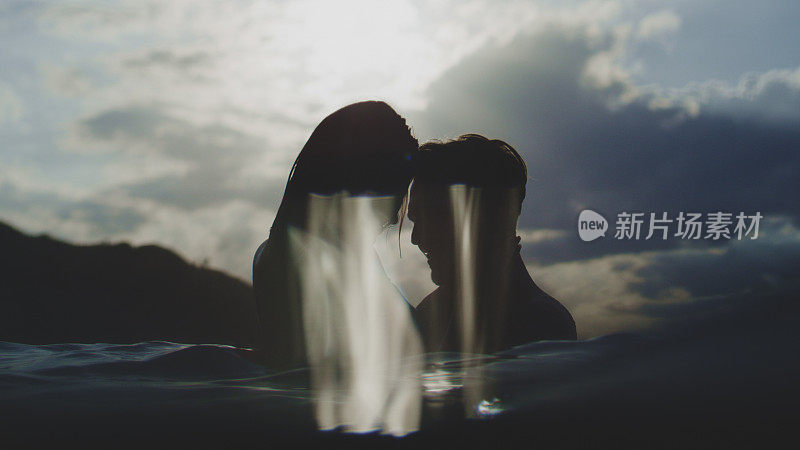 浪漫的异性情侣在日落时分一起在海里游泳。玩耍和亲吻