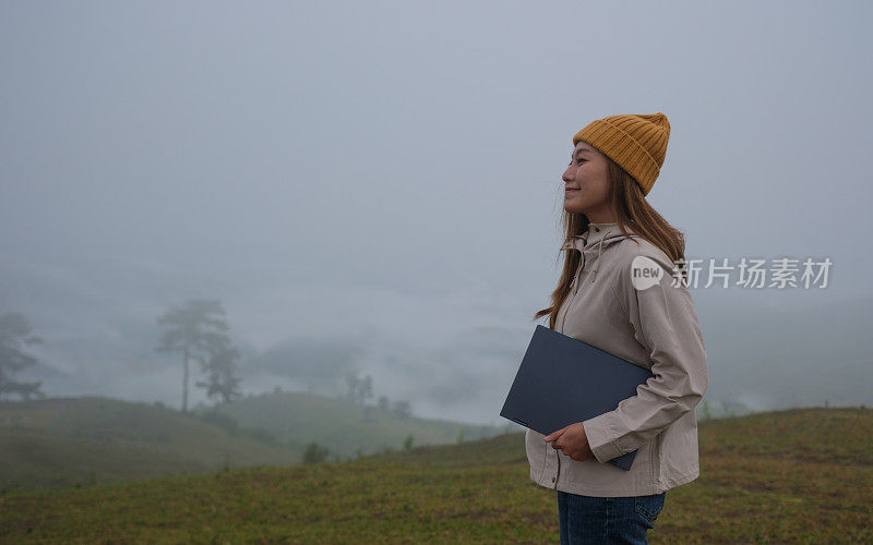 在大雾天，一位女性旅行者在山中旅行时抱着笔记本电脑的特写