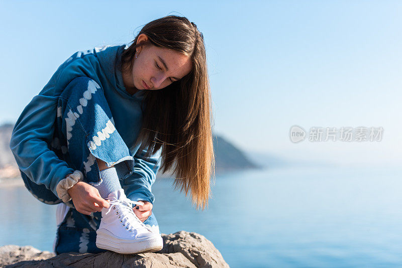 十几岁的女孩在一个阳光明媚的冬日在海边系白色运动鞋