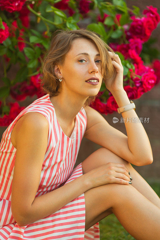 金发女人在背景上的玫瑰灌木。花园。春天的背景