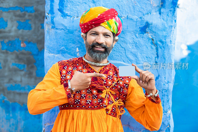 快乐的传统印度人戴着彩色的头巾和服装，展示借记卡的广告或品牌。胡子男手持空商务卡或电子卡进行支付，实物模型。