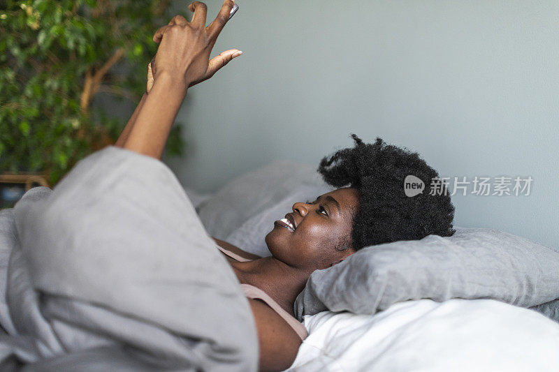 年轻的黑人女性在床上使用手机