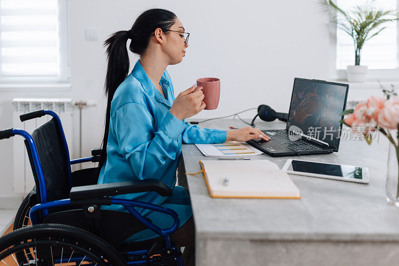 坐轮椅的女人一边喝咖啡，一边用笔记本电脑工作