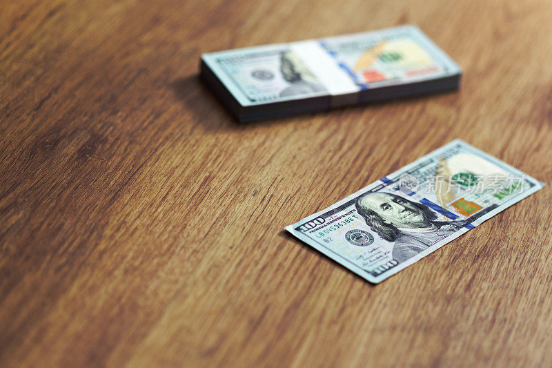 100美元的钞票散落在木质表面上，其中包括一捆用货币带包裹的钞票