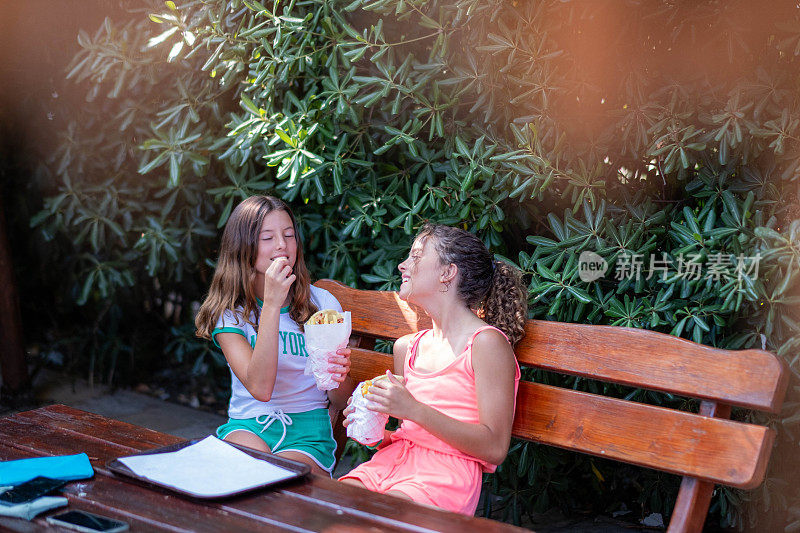 两个十几岁的女孩在一家餐馆里，边吃午饭边聊天，笑着，玩得很开心。