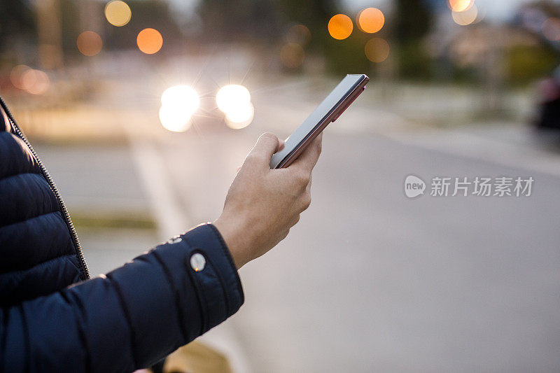 年轻女子站在人行道上，通过智能手机上的移动应用程序叫出租车