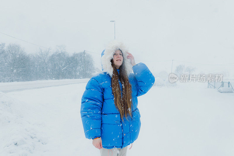 在大雪中漫步在斯堪的纳维亚村庄的街道上，穿着蓝色外套欣赏冬日童话的女人