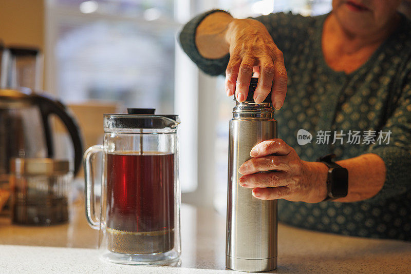 老年妇女的手与保温杯绝缘饮料容器，优先考虑持久的温暖为茶。