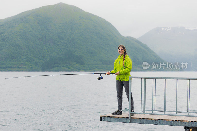 身穿绿夹克的女子在挪威峡湾钓鱼