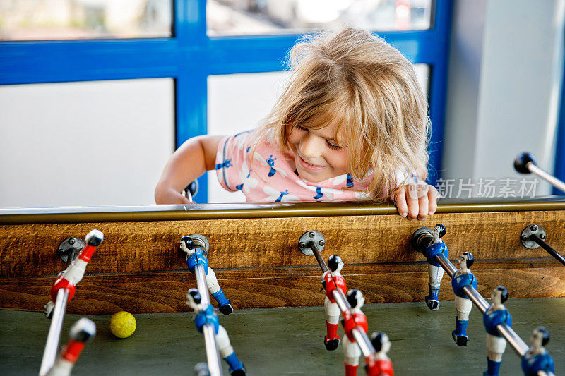 幼儿园的小女孩在玩桌上足球。快乐、兴奋、积极的孩子与兄弟姐妹或朋友一起玩家庭游戏。