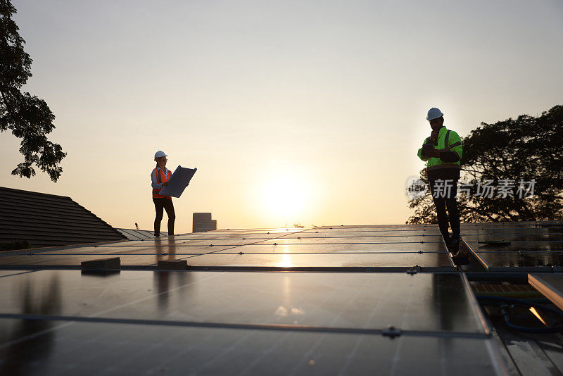 剪影网站太阳能服务工程师团队在太阳能屋顶上对着夕阳工作