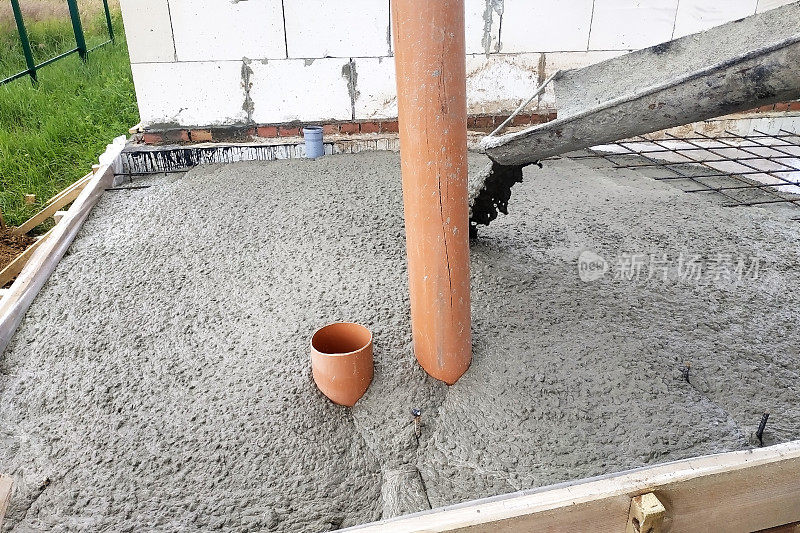 混凝土搅拌机通过排水沟向混凝土板注入水泥，下水道管道清晰可见。