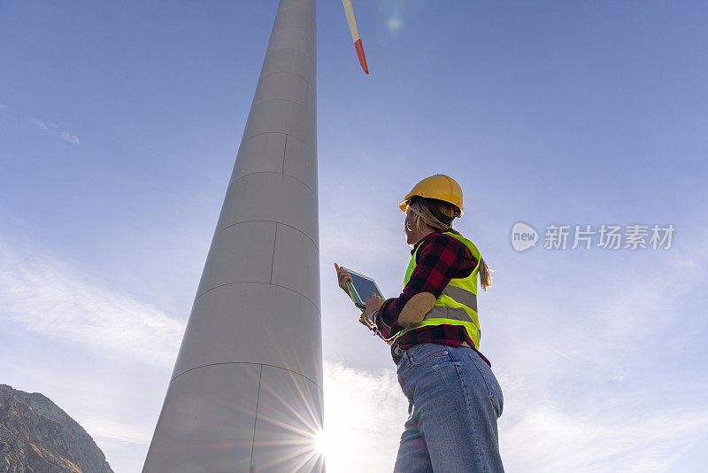 一名女工程师正在检查用于可再生能源生产的风力涡轮机基础设施，她正在使用数字平板电脑记录现场数据