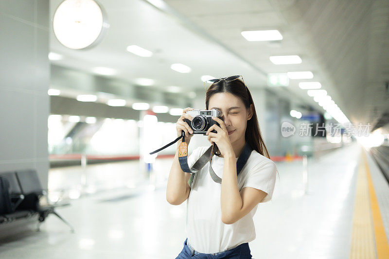 一位亚洲女性背包客在火车站用相机拍照。