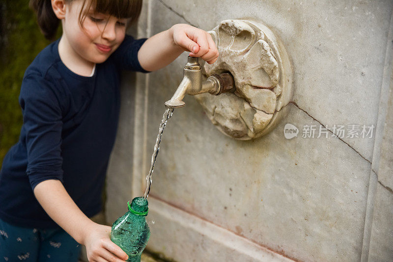 一个小女孩在公共水龙头旁装满了一瓶水