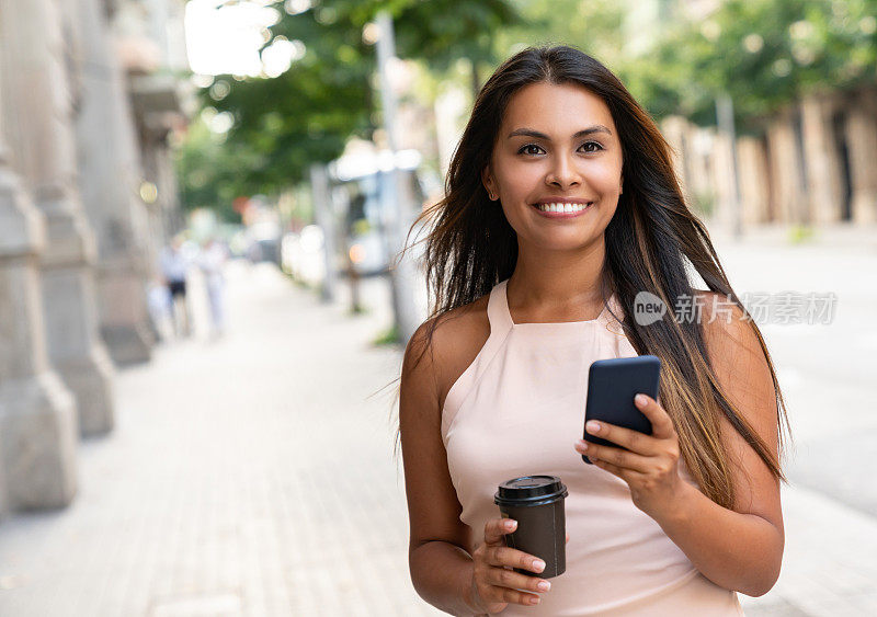 一个女人一边用手机发短信一边在街上喝咖啡