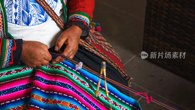秘鲁妇女的手使羊驼毛地毯与民族图案的特写。秘鲁库斯科生产羊毛材料。身着鲜艳传统秘鲁服饰的女子