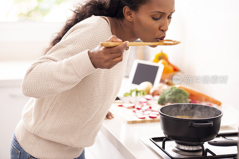 近距离女子品尝汤与木勺在厨房。