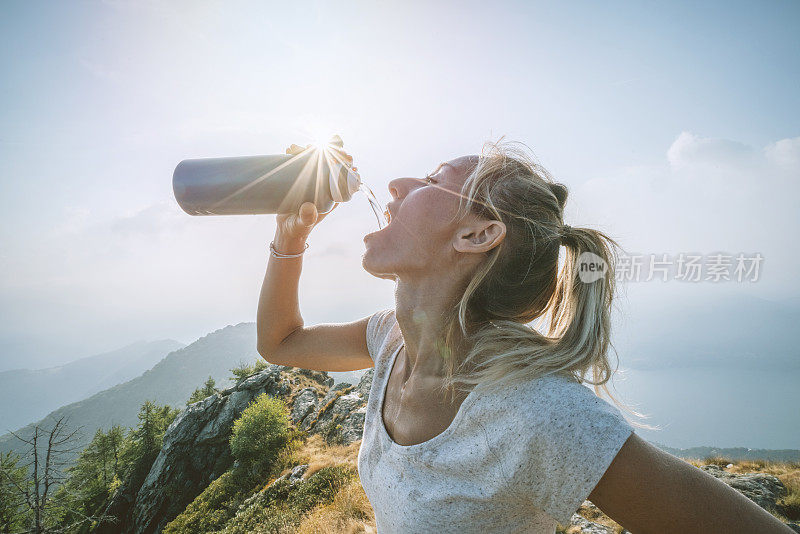 徒步旅行的女人用水瓶在山路上喝水