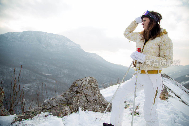 近景美丽的年轻女子在冬天的衣服站在一边，手拿木棍的背景雪山