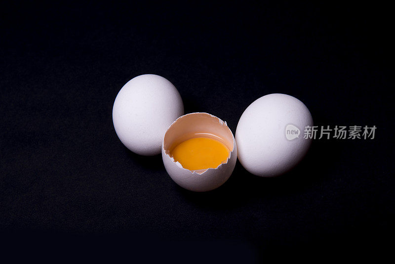 高角度的小组白色生鸡蛋，一个是破在黑色的背景