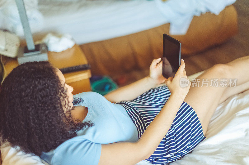 30多岁的混血女性在卧室里使用电子平板电脑