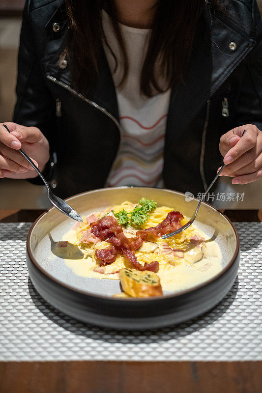 年轻的亚洲女人正在吃意大利通心粉和脆培根