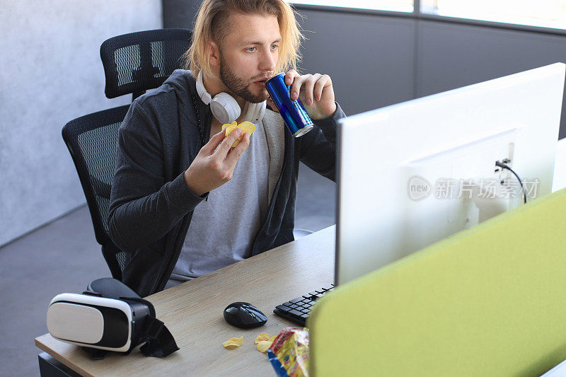 穿着休闲服装的专注的年轻人使用电脑，播放游戏或攻略视频，吃着薯条。