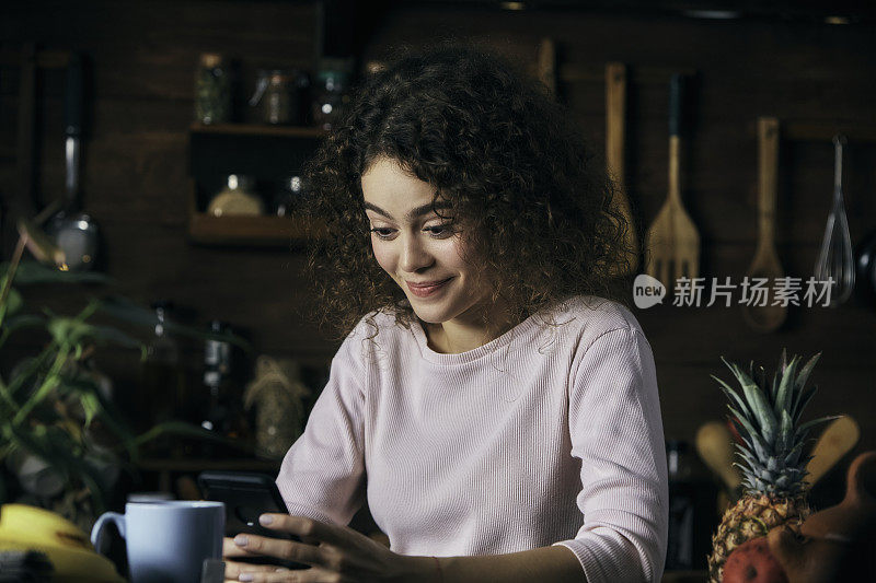 一个西班牙卷发的年轻女子在一个乡村厨房里用手机给一个朋友发短信