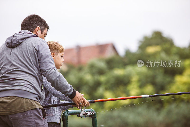 这是一副男人的样子，他在教一个男孩如何移动鱼竿