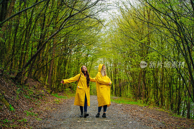 两个穿着雨衣的女性朋友在雾霾的森林里在雨中奔跑