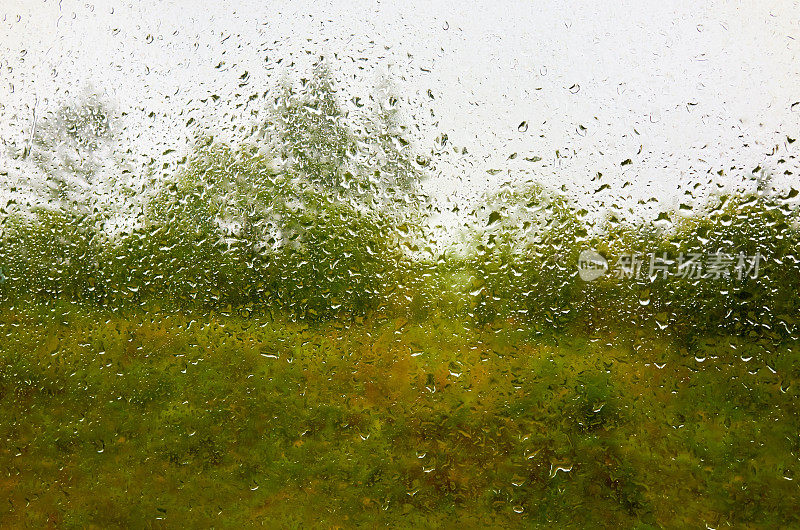 景观和多云的天空透过水滴雨潮湿的窗户