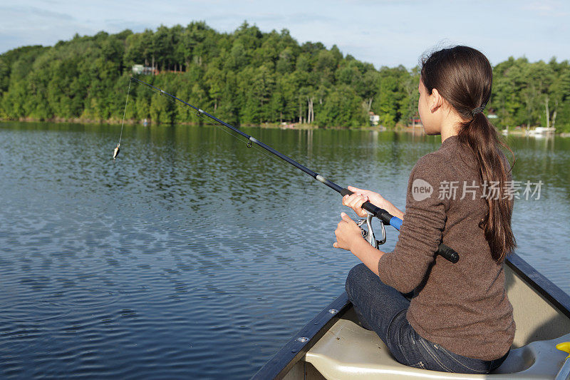 清晨的阳光下，女孩在湖上的独木舟上钓鱼