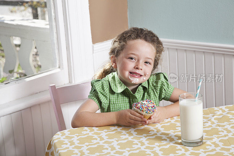 小女孩拿着一杯牛奶吃纸杯蛋糕