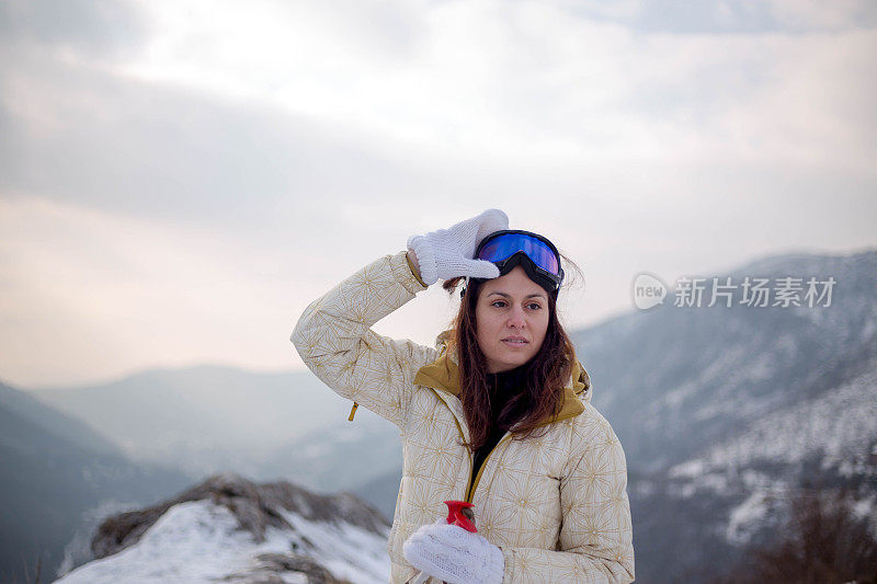 近景美丽的年轻女子在冬天的衣服站在一边，手拿木棍的背景雪山