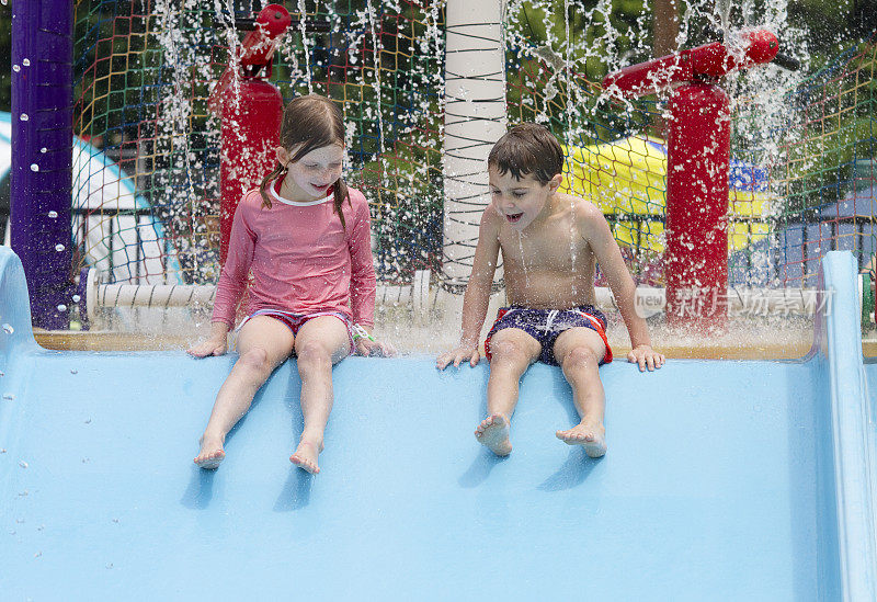 两个小孩在游泳池水上滑梯上游泳和玩耍