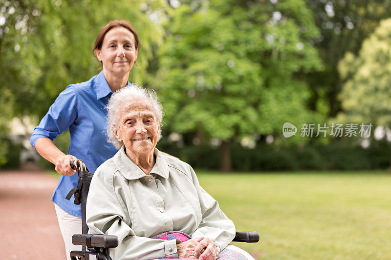 老女人坐在轮椅上和护理员在公园里