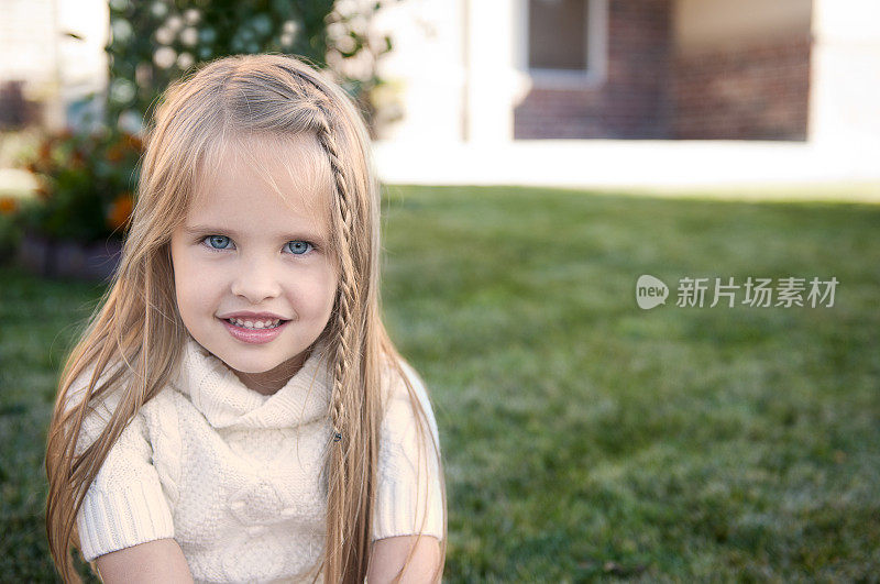 梳着辫子的小女孩坐在草地上微笑