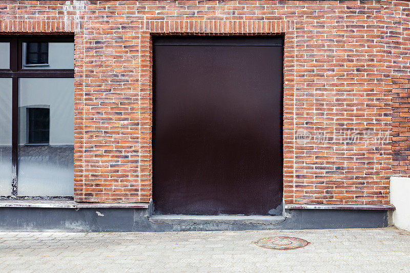 红色砖墙背景上封闭的金属门漆成棕色