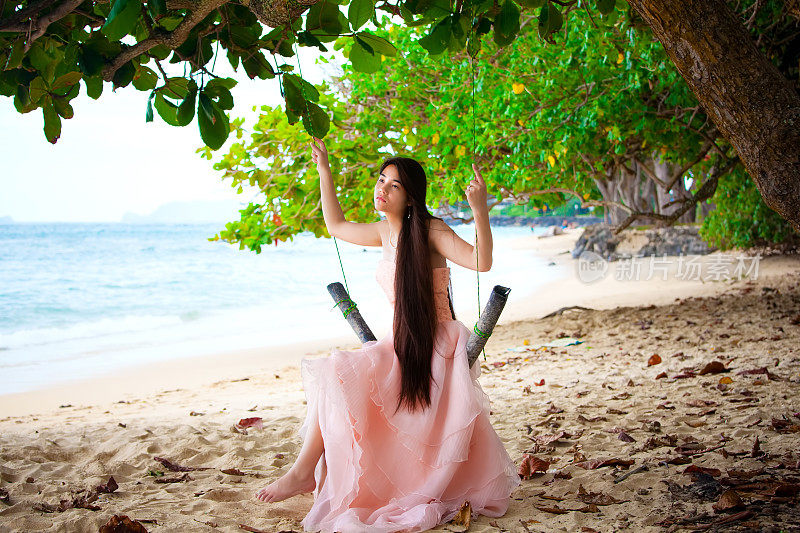 穿着粉红色裙子的少女坐在沙滩上的秋千上