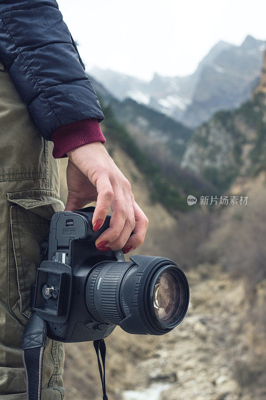 一位女性手持相机，背靠山景