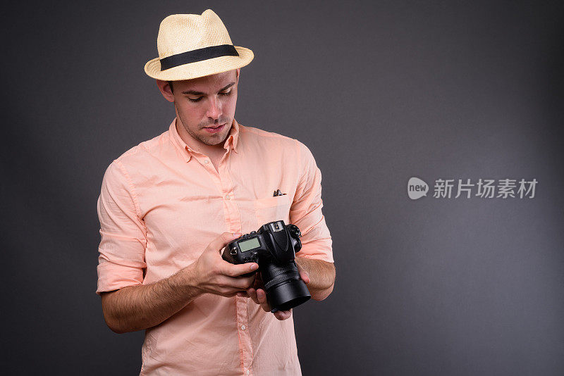 年轻英俊的游客带着照相机戴着帽子在灰色的背景下