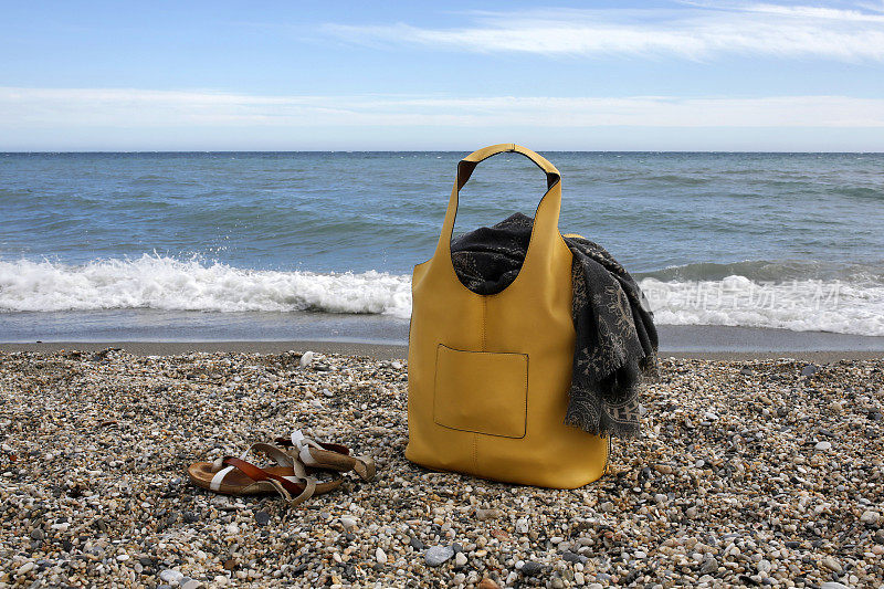 沙滩上的黄色皮包，围巾和凉鞋